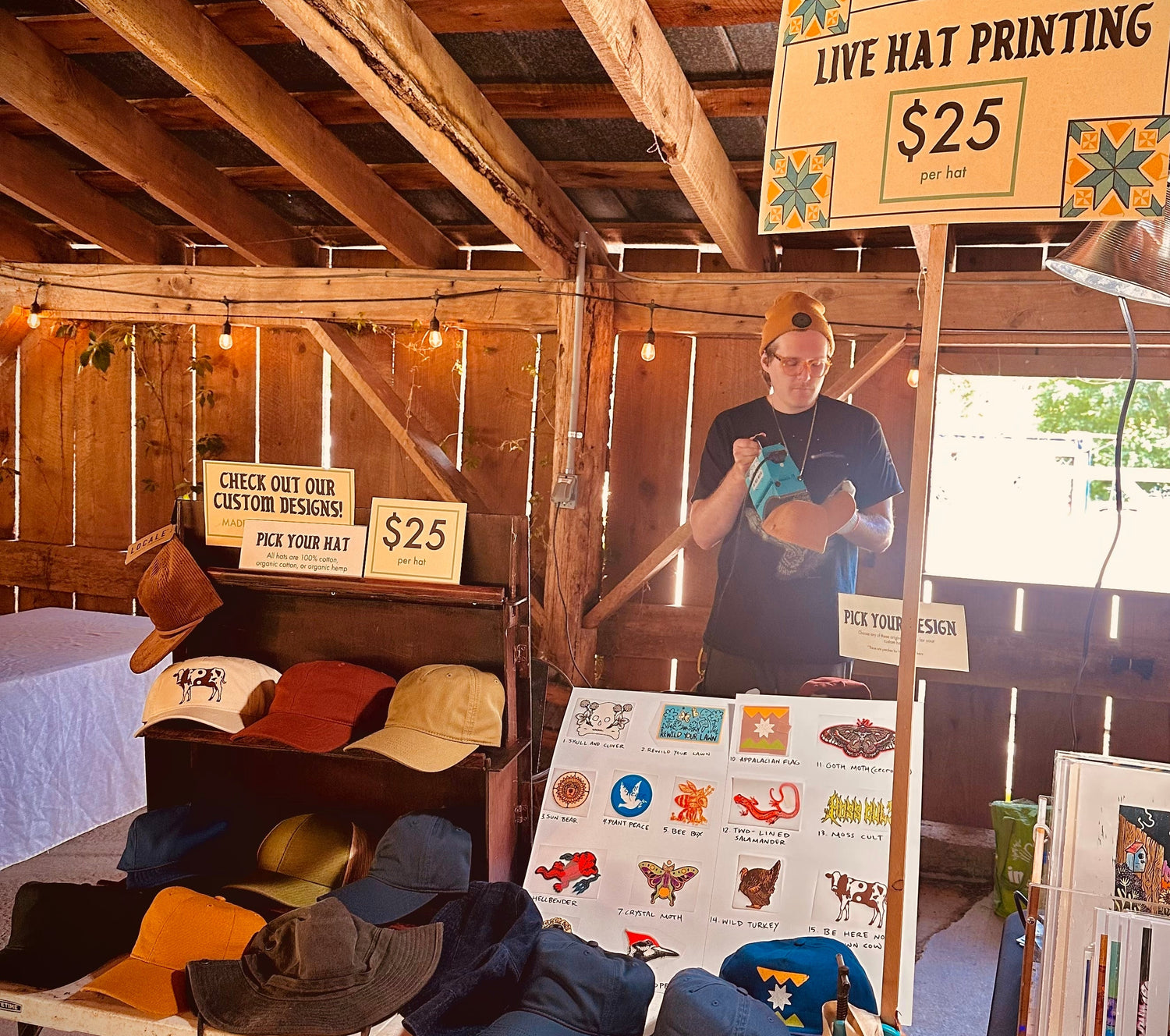 Person holding a hat with a sign for custom design printing in a rustic indoor setting.